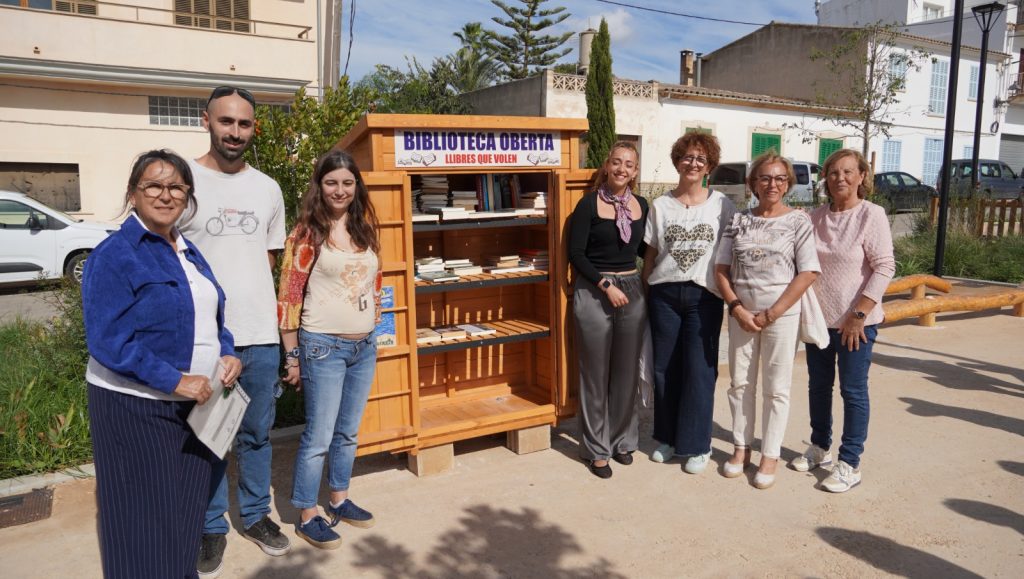 Casetes de fusta pintades amb llibres a dins, situades en una plaça de poble amb una església de pedra al fons